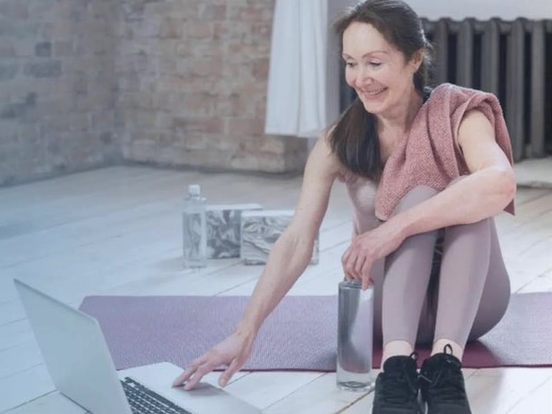 Ältere Frau trainiert zu Hause auf der Matte mit dem Laptop